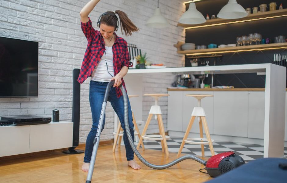 Spring Cleaning Tips by Just Rubbish Removal woman vacuuming and dancing with headphones on.