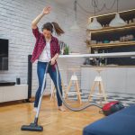 Spring Cleaning Tips by Just Rubbish Removal woman vacuuming and dancing with headphones on.