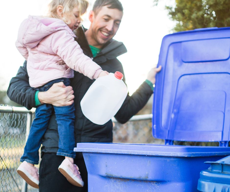 A man teaching his daughter to take out the trash and recycle